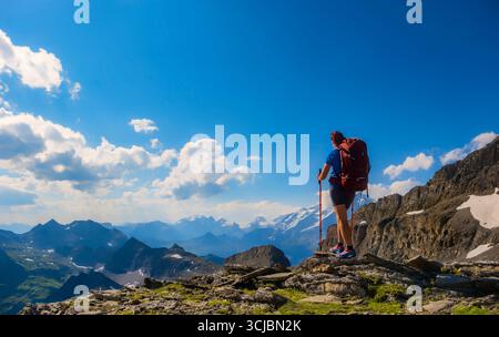 Un randonneur solitaire s'arrête sur un pic rocheux, contemplant le terrain montagneux à couper le souffle en contrebas. Femme sportive randonnant en Suisse alpes. Mode de vie hathique Banque D'Images