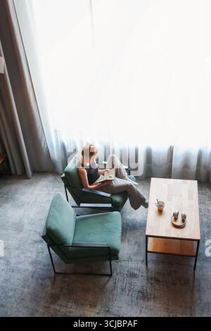 Week-end détente, femme profitant d'une pause café dans un salon lumineux. Banque D'Images