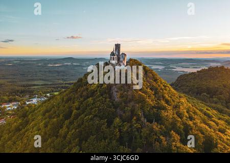 Le château de Bezdez se dresse majestueusement sur un pic rocheux entouré d'une végétation luxuriante pendant l'heure dorée de l'été. Le soleil se couche derrière la structure médiévale, renforçant son charme historique et sa beauté. Banque D'Images