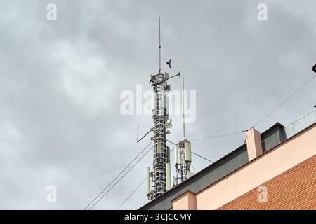 Vue rapprochée de deux antennes de télécommunication et d'une tour cellulaire sur le toit d'un bâtiment, face à un ciel couvert spectaculaire. Banque D'Images