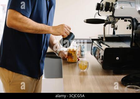 Un homme fait du café glacé dans un cadre de bureau, en utilisant une machine à café moderne. Cette configuration confortable inspire la productivité et offre une pause rafraîchissante pour Banque D'Images