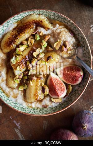 Vue de dessus d'un bol de petit déjeuner végétalien avec des bananes caramélisées, des figues fraîches et des pistaches sur flocons d'avoine crémeux, sur un fond de bois rustique Banque D'Images