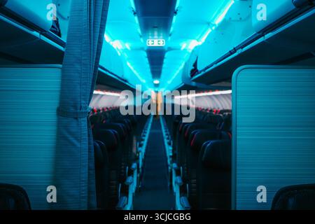 Une vue à l'intérieur d'une cabine d'avion commercial avec des rangées de sièges vides sous un éclairage bleu ambiant. Les compartiments supérieurs sont fermés, créant un calme Banque D'Images