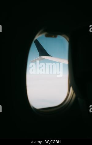 Vue d'une fenêtre d'avion montrant l'aile de l'avion contre un ciel bleu clair. L'image capture le sens du voyage et l'expérience de voler un Banque D'Images