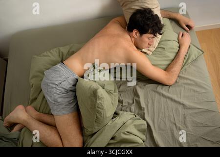 Un jeune homme se repose paisiblement sur un lit confortable. La scène capture un moment de tranquillité et d'apathie, dans le calme d'un décor matinal Banque D'Images