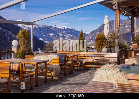 Un restaurant autrichien accueillant en terrasse situé dans les Alpes enneigées en hiver. Des bancs en bois confortables avec des jetés de fourrure offrent chaleur et charme contre une race Banque D'Images