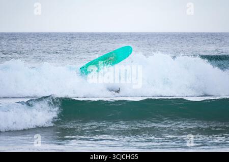 Un surfeur tombe d'une planche de surf aquatique lors d'un wipout dans les vagues de Zarautz, pays Basque, Espagne, capturant l'énergie dynamique et le mouvement du Banque D'Images