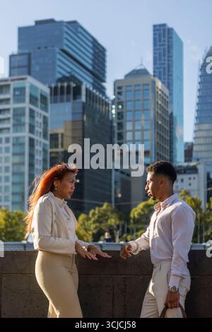 Deux professionnels s'engagent dans une conversation d'affaires à l'extérieur avec le paysage urbain de Melbourne en arrière-plan. La scène reflète le mode de vie urbain et le mode Banque D'Images