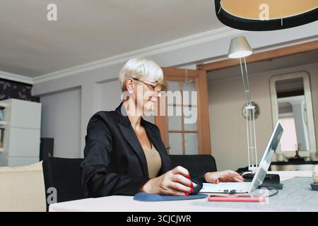 Une femme professionnelle travaille sur son ordinateur portable dans un environnement de bureau à domicile moderne. Elle est concentrée et productive, incarnant le style de vie du travail à distance dans un style Banque D'Images