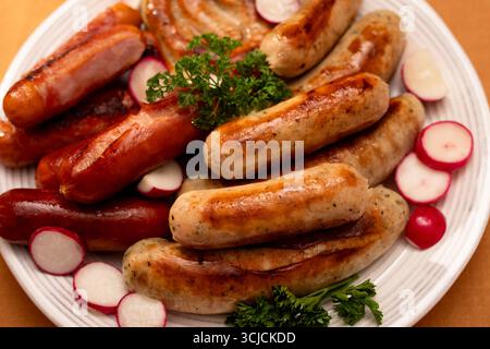 Vue de dessus d'un plateau présentant diverses saucisses grillées allemandes, y compris bratwurst et bockwurst, garni de persil frais et de radis tranchés Banque D'Images