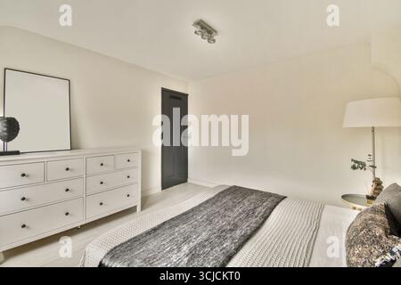 Une chambre minimaliste avec une élégante commode blanche avec six tiroirs, une lampe élégante et une porte noire. La literie texturée apporte confort et chaleur Banque D'Images