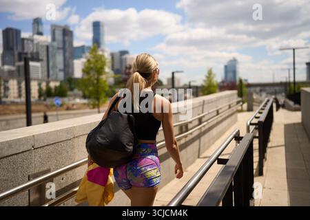 Femme vêtue de vêtements d'activité marche le long d'un sentier urbain, capturant l'essence de la vie urbaine et de la forme physique en plein air. L'horizon de la ville forme un impressionnant Banque D'Images