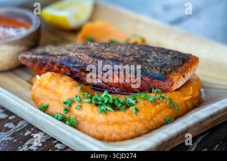 Filets de saumon frits servis avec garniture de légumes sur assiette en bois et sauce, gros plan. Filet de saumon rôti avec purée de patates douces. Banque D'Images