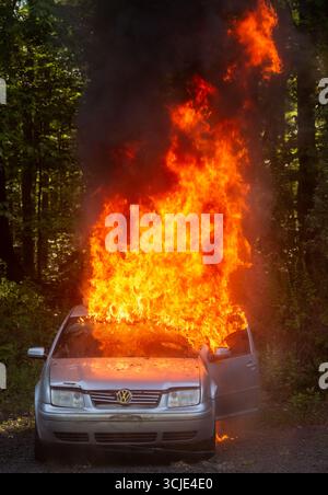 Les pompiers combattent un feu de voiture flamboyant avec une fumée et des flammes abondantes, mettant en valeur les interventions d'urgence, la sécurité incendie et des actions de sauvetage spectaculaires. Banque D'Images