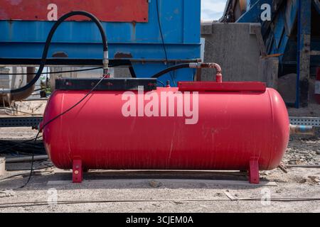 Grand réservoir rouge de compresseur d'air industriel avec des tuyaux connectés sur le chantier de construction extérieur avec le béton et le fond de machines Banque D'Images