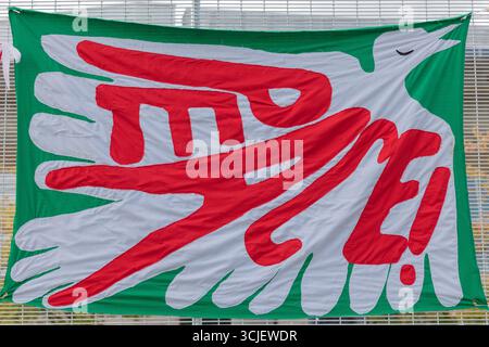 Londres, Royaume-Uni. 6 septembre 2025. Une colombe blanche stylisée avec des marques rouges est représentée en vol sur une bannière verte, symbolisant la paix ou la protestation. La bannière est fixée à une clôture métallique, suggérant une exposition publique lors d'une démonstration ou d'un événement. Arrêtez le camp de paix Arms Fair aux portes de l'entrée est d'Excel dans les docklands de Londres. Le site accueille actuellement l'exposition bisannuelle Defence and Security Equipment International (DSEI). Penelope Barritt/Alamy Live News Banque D'Images