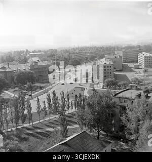 Une vue panoramique d'une intersection dans le secteur de la rue Yunykh Kommunarov (aujourd'hui rue Bankivska) à Slavyansk, prise dans la seconde moitié des années 1970 Ce paysage urbain de l'ère de la stagnation démontre l'harmonie d'une ville industrielle : des rues immergées dans la verdure avec l'architecture de l'ère stalinienne et le transport soviétique contre un horizon industriel avec des cheminées d'usine, symbolisant la vie mesurée d'un Donbass paisible Banque D'Images