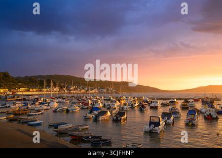 Lyme Regis, Dorset, Royaume-Uni. 7 septembre 2025. Météo britannique : le ciel au-dessus du port de Cobb brille de couleurs éclatantes glorieuses tandis que la station balnéaire de Lyme Regis se réveille avec un spectaculaire lever de soleil vibrant et sombre devant de fortes pluies d'orage. Le dicton « ciel rouge dans l'avertissement du berger du matin » semblait approprié alors que le ciel s'illuminait d'une couleur glorieuse et enflammée et d'un nuage sombre inquiétant. Crédit : Celia McMahon/Alamy Live News Banque D'Images