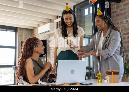 Collègues portant des chapeaux de fête célébrant avec des cadeaux et des rires dans un bureau moderne Banque D'Images