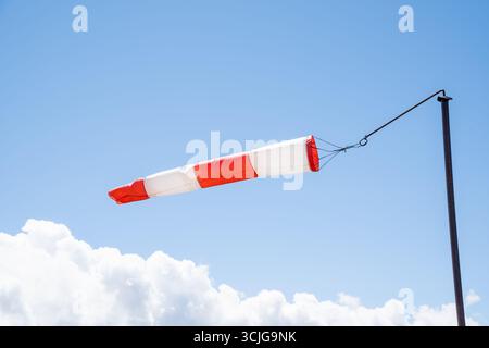 Chaussette rayée rouge-blanc contre un ciel bleu clair avec des nuages blancs moelleux en été comme indication pour le vent soufflé Banque D'Images