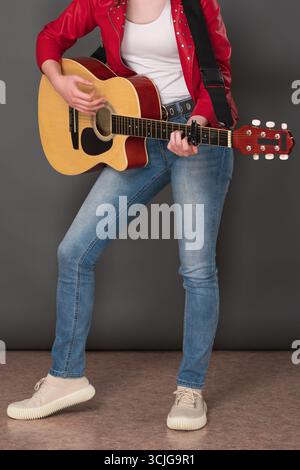 Vue avant de la section basse de guitariste femme méconnaissable jouant de la guitare acoustique à six cordes. Jeune musicienne élégante est habillée en cramoisi le Banque D'Images