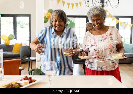 Des femmes souriantes appréciant des boissons et des collations à la maison pendant la célébration festive Banque D'Images