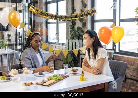 Célébrant l'anniversaire au bureau, deux femmes appréciant les collations et la conversation Banque D'Images