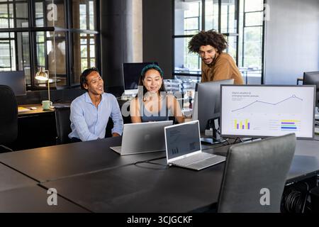 Équipe collaborant dans le bureau moderne, analysant les graphiques sur les ordinateurs portables et le moniteur Banque D'Images