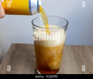 Une canette de bière étant versée dans un grand verre avec de la mousse se formant sur le dessus sur un fond de table en bois Banque D'Images