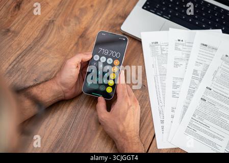 Les contribuables matures comptent leurs finances sur leur smartphone en travaillant avec des formulaires fiscaux sur la taxation des bureaux en bois Banque D'Images