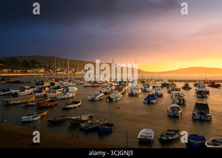 Lyme Regis, Dorset, Royaume-Uni. 7 septembre 2025. Météo britannique : le ciel au-dessus du Cobb brille d'une couleur éclatante glorieuse tandis que la station balnéaire de Lyme Regis se réveille avec un spectaculaire lever de soleil vibrant et sombre devant de fortes pluies de tonnerre. Le dicton « ciel rouge dans l'avertissement du berger du matin » semblait approprié alors que le ciel s'illuminait d'une couleur glorieuse et enflammée et d'un nuage sombre inquiétant. Crédit : Celia McMahon/Alamy Live News Banque D'Images