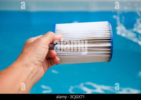Cartouche filtrante de piscine de remplacement dans la main d'une femme sur le fond de piscine de famille bleue. Réutilisation du filtre. Banque D'Images