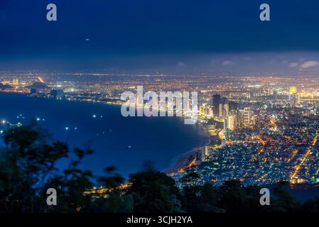 Vue panoramique de Da Nang la nuit depuis Ban Co Peak, avec des lumières étincelantes de la ville, des gratte-ciel, des ponts illuminés sur la rivière Han, et Banque D'Images