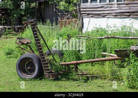 Matériel agricole. Herse métallique, deux roues dans l'herbe. Vieille ferme abandonnée. Banque D'Images