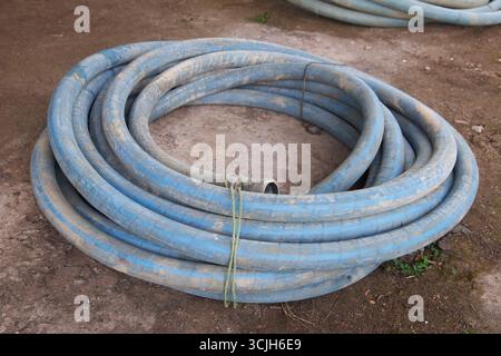 tuyau robuste bleu enroulé couché sur le sol extérieur, se connecte au compresseur et à la perceuse dans l'industrie des puits tubulaires, soft focus dans le flou Banque D'Images