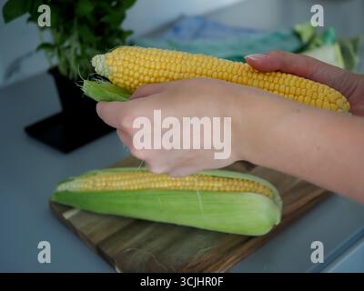 Gros plan des mains préparant le maïs frais sur la planche à découper pour la cuisson Banque D'Images