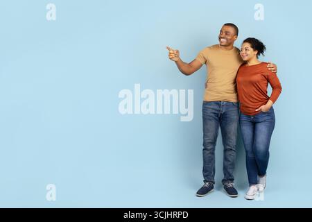 Couple afro-américain souriant debout côte à côte, pointant vers l'avant Banque D'Images