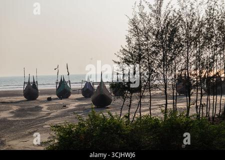 Bateaux de pêche colorés traditionnels alignés gracieusement sur une vaste rive de sable avec un fond bleu de mer sans fin. Banque D'Images