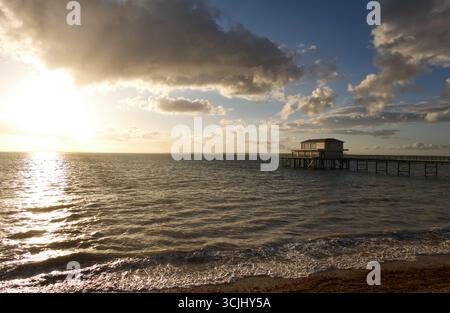 Totland Pier, Totland Bay, île de Wight, Angleterre, Royaume-Uni - la jetée victorienne vue au coucher du soleil avec un éclat de soleil sur la mer et des vagues lançant sur la plage Banque D'Images