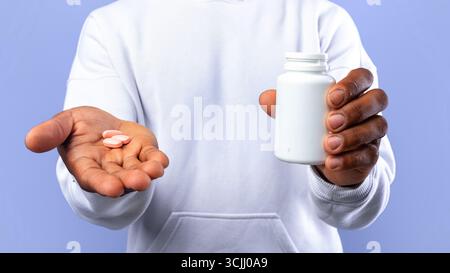 Adolescent noir méconnaissable contenant un pot avec des médicaments et des pilules dans les mains sur fond bleu.Coronavirus, rhume, traitement de la grippe Banque D'Images