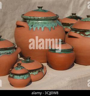 Une collection de pots traditionnels en argile de différentes tailles. Les pots ont un design rustique avec des accents verts et des couvercles. Ils sont disposés sur un backgrou neutre Banque D'Images