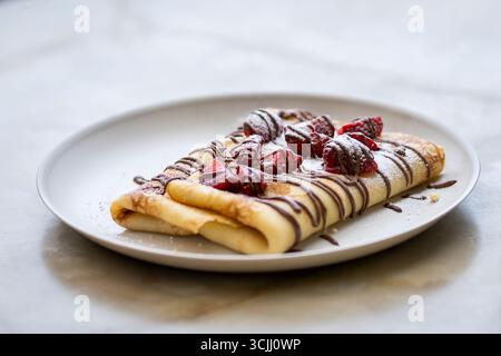 Délicieuse crêpe à la fraise et à la crème au chocolat dans l'assiette. Crêpes avec filet de chocolat et fraises fraîches sur une assiette. Banque D'Images