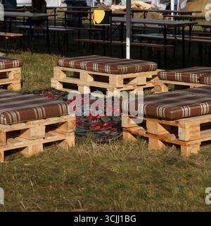 Palettes en bois disposées comme des sièges avec des coussins rayés sur une zone herbeuse. Idéal pour les rassemblements ou événements extérieurs Banque D'Images