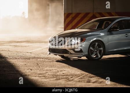 Volvo S60 garé sous un pont. Partie avant de la berline argentée dans les rayons du soleil couchant, piliers en béton à l'arrière-plan, l'air est rempli de poussière ou Banque D'Images