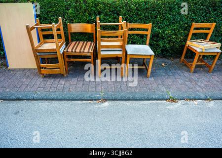 Vieilles chaises en bois et un meuble laissé sur le trottoir à côté d'une haie, peut-être en attente de collecte des ordures ou de réutilisation Banque D'Images