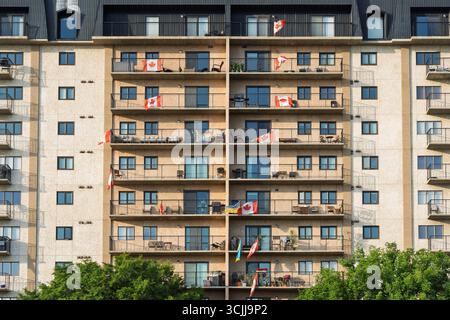 Bâtiment haut avec balcons et drapeaux sur le toit. Les drapeaux viennent du Canada. Le bâtiment est très grand et a de nombreuses fenêtres Banque D'Images