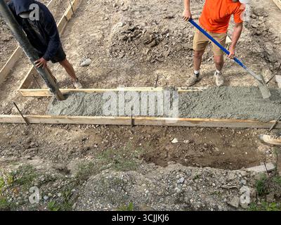 Deux ouvriers et une pompe à béton coulent activement du ciment dans une forme en bois. Banque D'Images