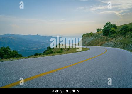 Route asphaltée sinueuse pittoresque dans les montagnes grecques avec vue panoramique sur les collines et les crêtes stratifiées sous le ciel calme du coucher du soleil Banque D'Images