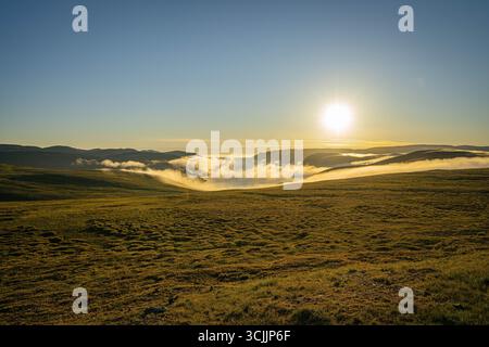 Le soleil de minuit brille sur les collines vallonnées de la toundra avec un faible brouillard dérivant à travers les vallées dans le paysage d'été près du Cap Nord de la Norvège Banque D'Images
