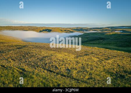Lumière dorée au-dessus des collines de toundra avec des parcelles de faible brouillard roulant à travers les vallées dans le paysage d'été arctique près de North Cape, au nord de la Norvège Banque D'Images